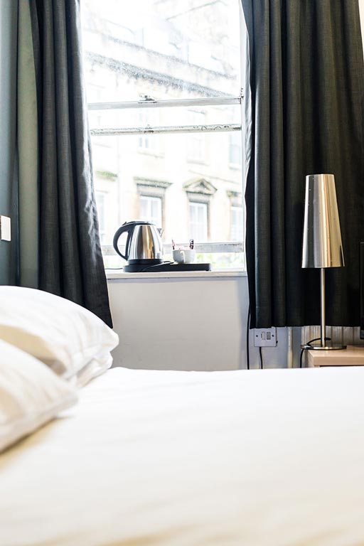 a double bed with a window next to it with Georgian buildings outside and a kettle and tea cup on the windowsill